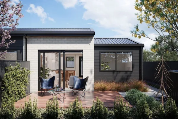 Outside view of one of the Spreydon units. There is a white brick feature wall contrasted with black wood cladding, and a wooden patio surrounded by an easy care garden.