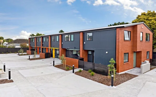 Photo of the units of the Dunkik development. The exterior of the units is navy and burnt orange, and there is a wide driveway with lanterns and a tidy garden in the front.