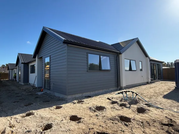 An exterior view of Evergreen House. The cladding is a dark grey and the ground is being prepared for landscaping.
