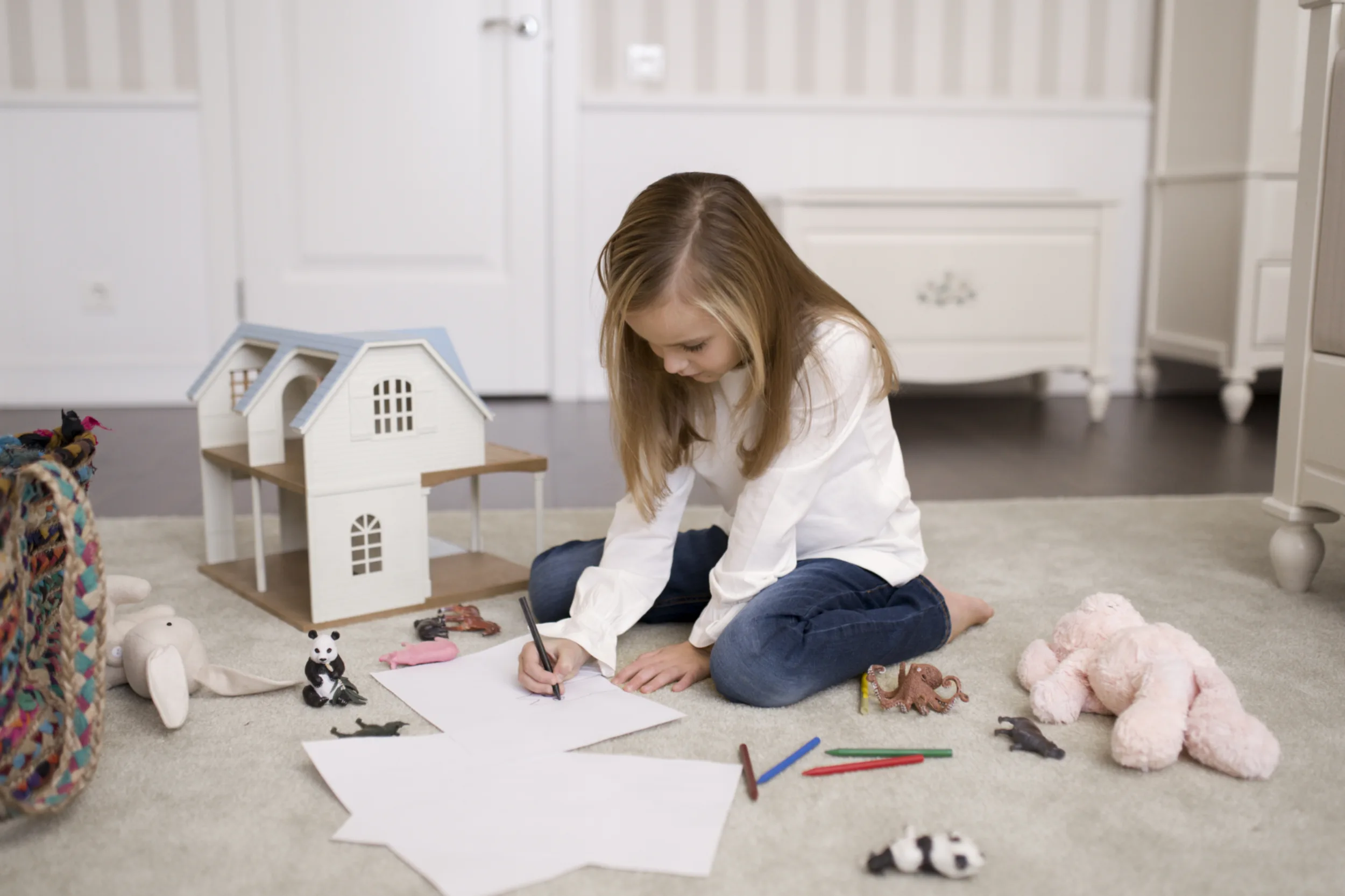 A little girls playing with a doll house and drawing.