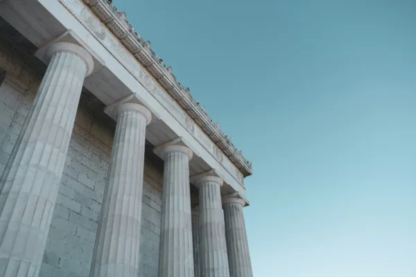 The corner of a grand concrete building against a blue sky, with five large pillars.