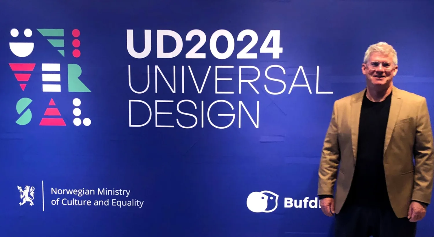 Image of Geoff at the UD2024 conference, He is wearing a tan suit jacket and a black t-shirt.